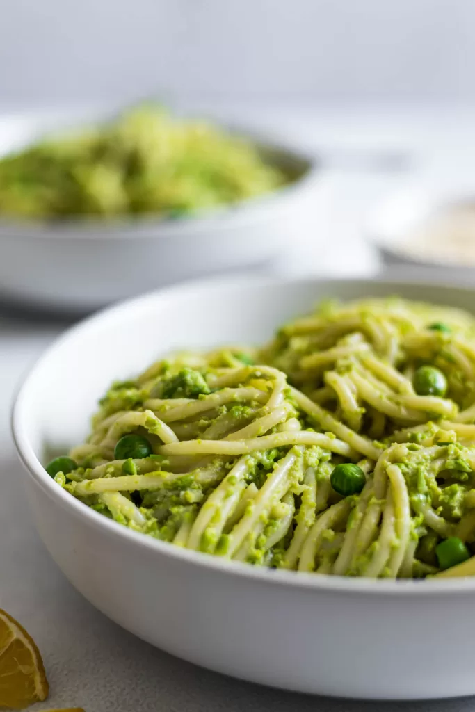 A side view of a bowl of green pea pasta with another bowl behind it.