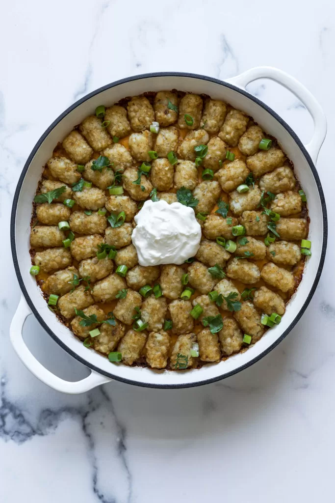 An overhead view of the tater tot casserole in a white braiser.