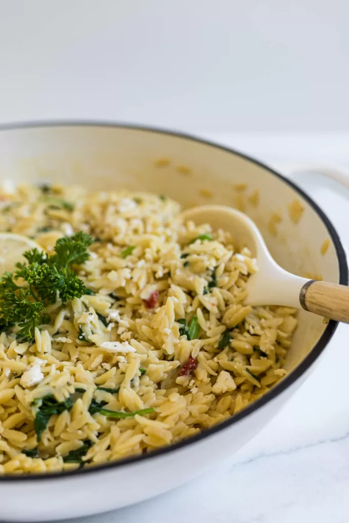 A side view of orzo in a pan with a serving spoon in it.