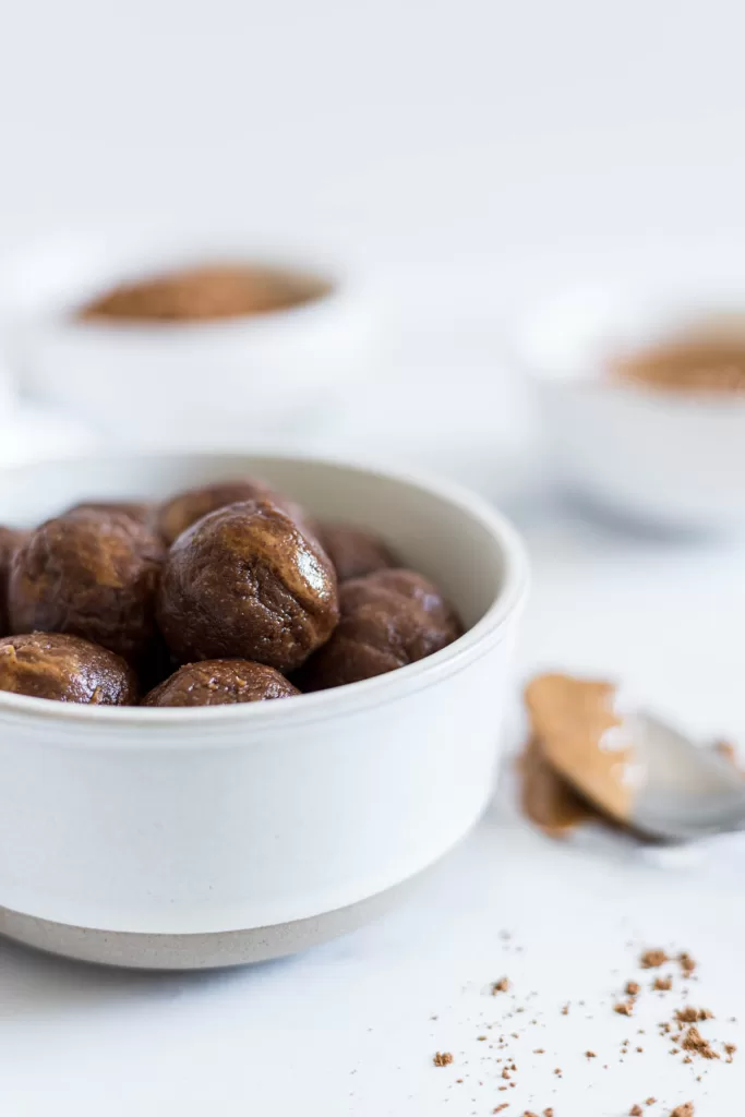 A side view of the Chocolate Almond Balls in a bowl with a spoonful of peanut butter next to it.