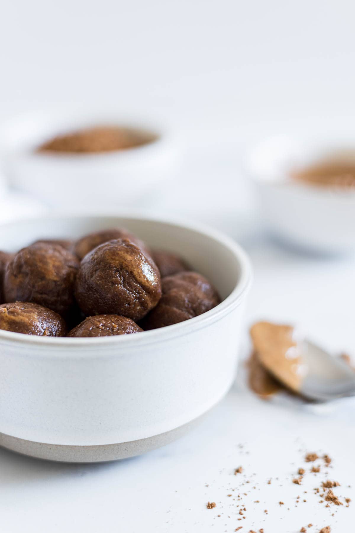A side view of the Chocolate Almond Balls in a bowl with a spoonful of peanut butter next to it.