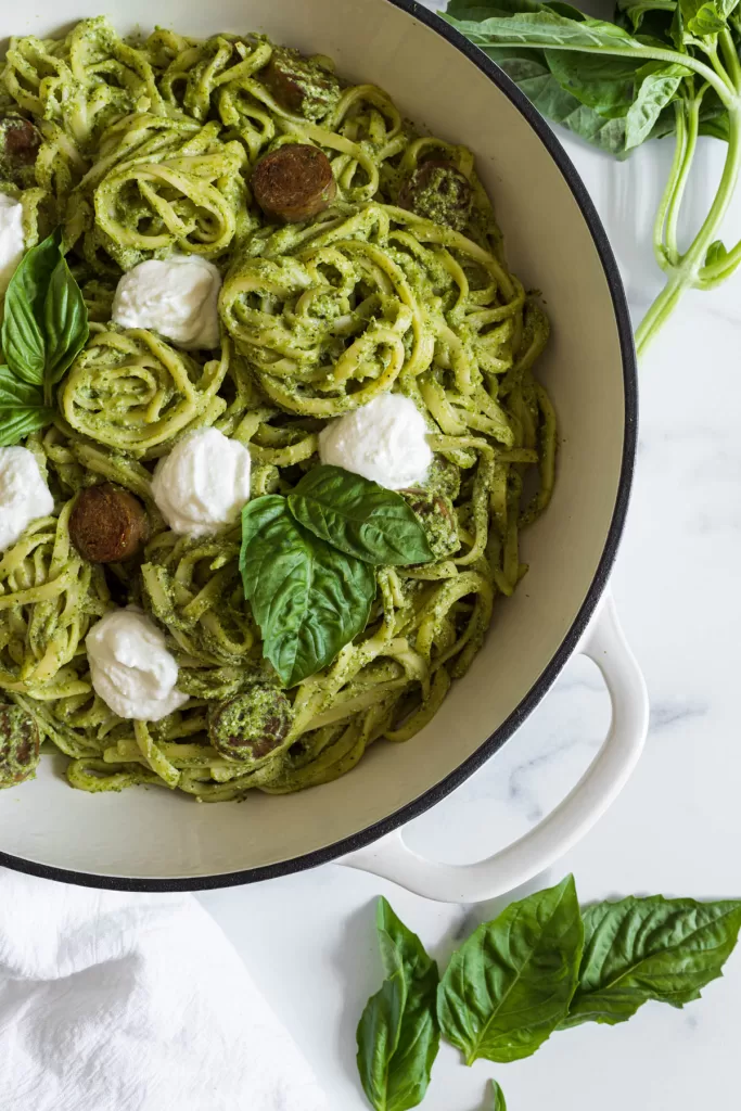 Pesto pasta in a braiser with basil surrounding it. 