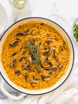 A braiser with pumpkin and mushroom risotto in it. A bottle of white wine is next to it.