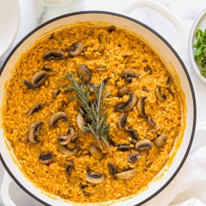 A braiser with pumpkin and mushroom risotto in it. A bottle of white wine is next to it.