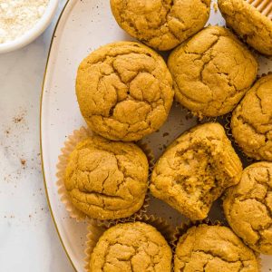 Overhead view of a plate of Gluten-Free Pumpkin Banana Muffins. One muffin has a bite out of it.