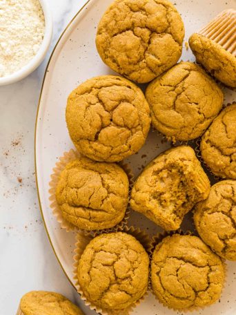 Overhead view of a plate of Gluten-Free Pumpkin Banana Muffins. One muffin has a bite out of it.