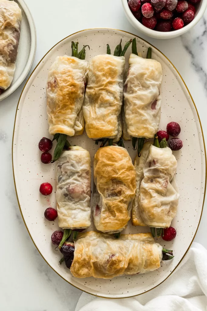 An overhead view of green bean bundles on a plate with cranberries scattered in between each bundle.
