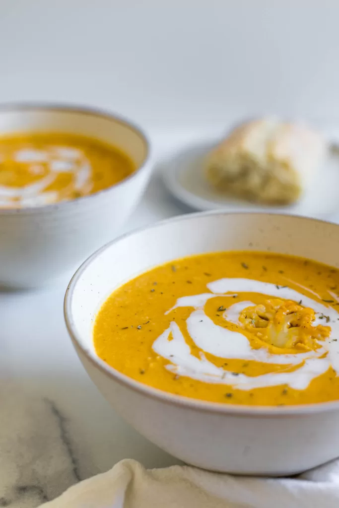 Two bowls of pumpkin soup with a piece of bread in the background.