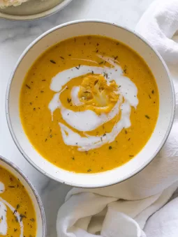 Overhead view of a bowl of pumpkin and cauliflower soup with coconut milk swirled in the soup and a piece of cauliflower set in the middle.