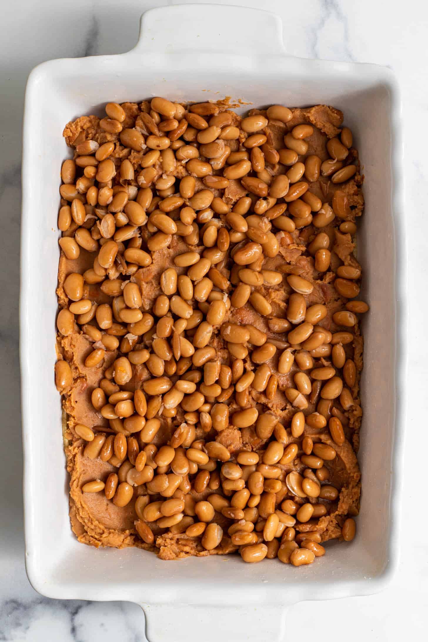 A baking dish with layers of refried beans and pinto beans.