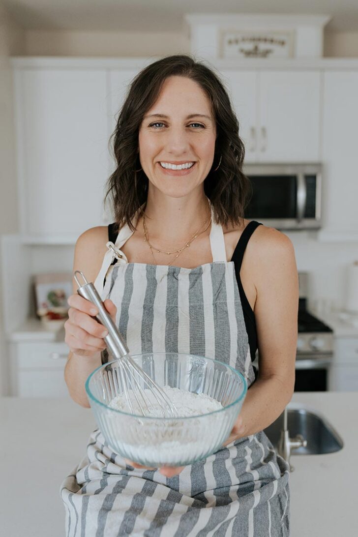 Kaileigh wearing an apron holding a bowl of flour.