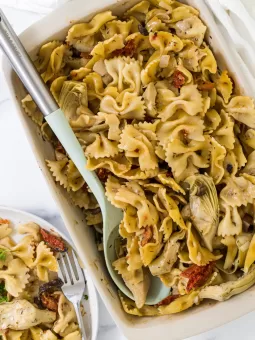 Artichoke and sun-dried tomato pasta in a baking dish with a serving spoon in it.