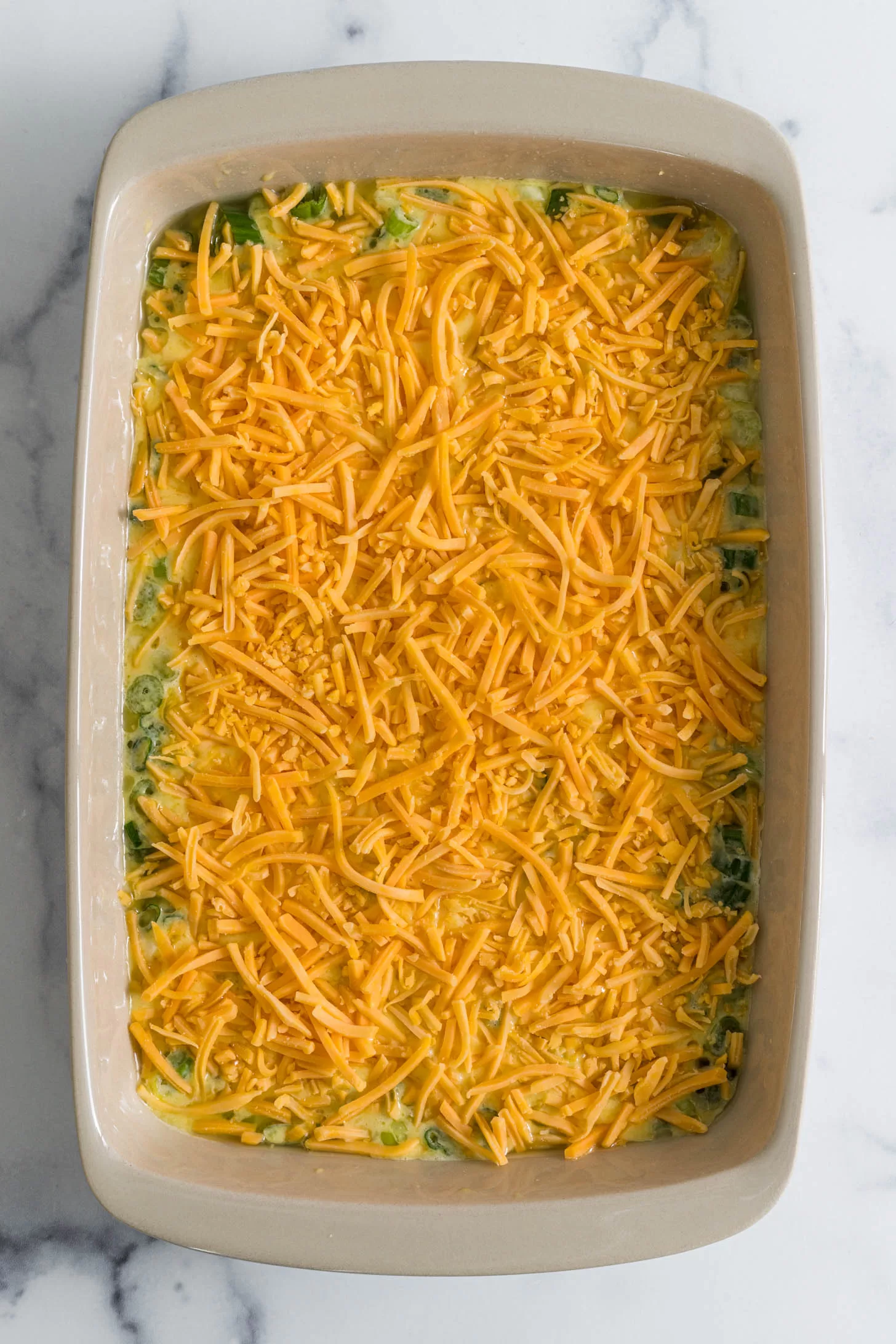 Egg mixture poured into baking dish with sprinkled cheese on top.