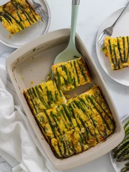Asparagus egg casserole in a baking dish with a serving utensil taking a slice out.