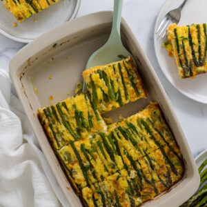 Asparagus egg casserole in a baking dish with a serving utensil taking a slice out.