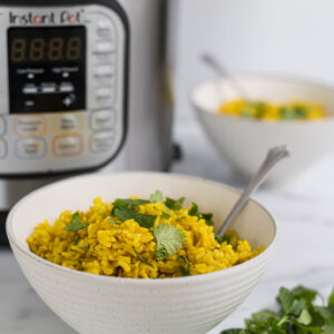 Turmeric Rice in a bowl with the Instant Pot behind it.