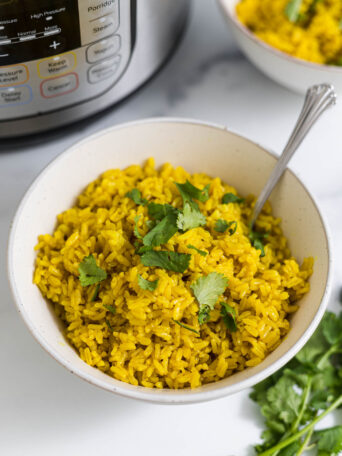 A bowl of turmeric rice with and Instant Pot behind it.