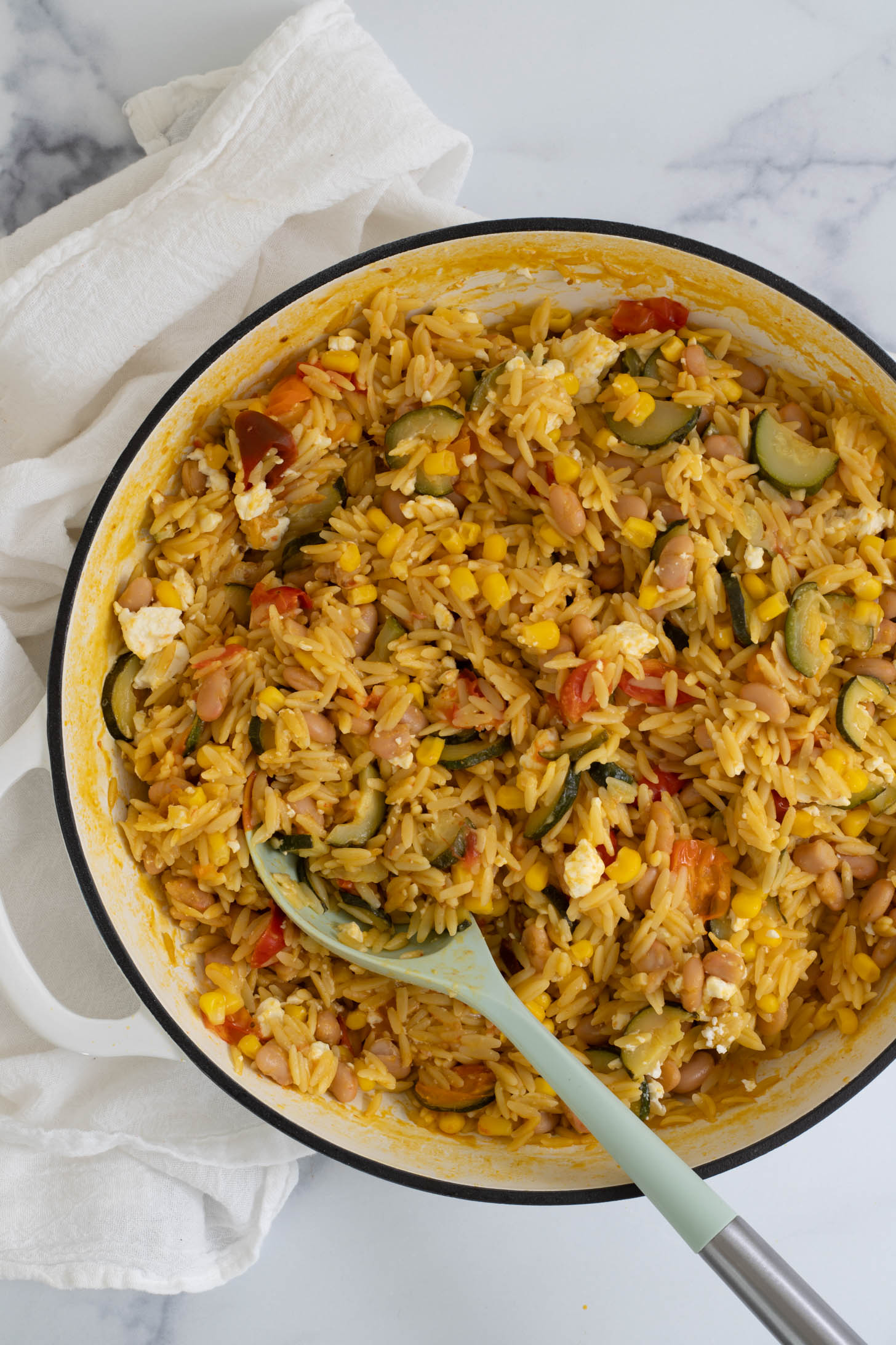 One pot orzo in a braiser with a serving spoon in it.