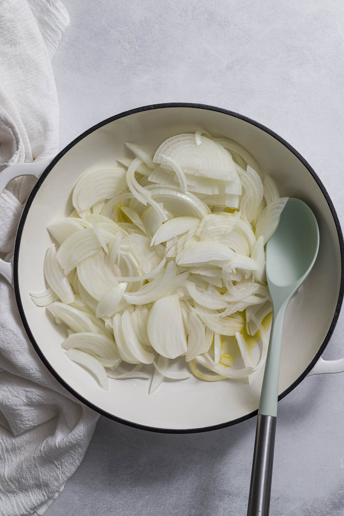 Onions being sauteed in a braiser with a spoon in it.