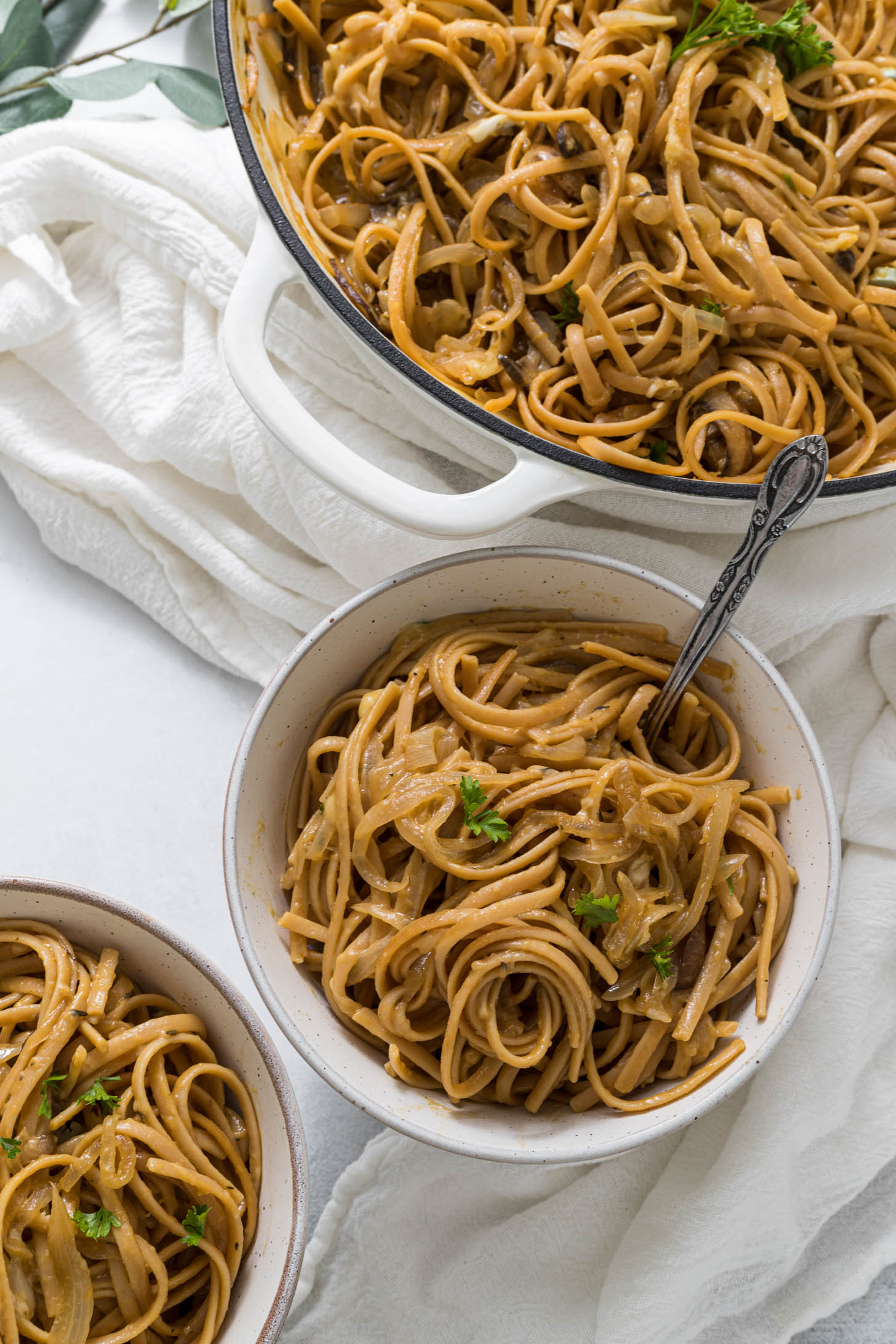 Overhead view of two bowls of one pot french onion pasta, with a braiser full of pasta sitting to the side of the bowls.