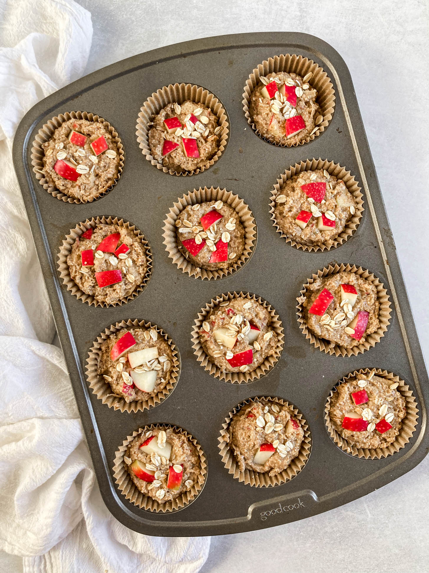 Muffin batter in a muffin tin, topped with apple chunks.