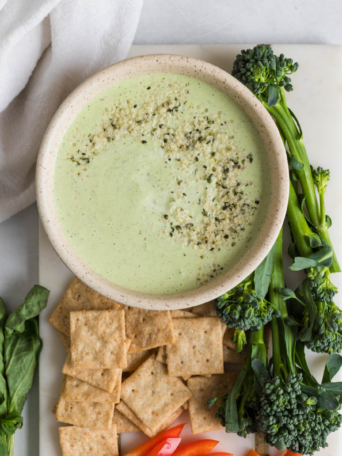 A bowl of green goddess dip with crackers and veggies next to it.